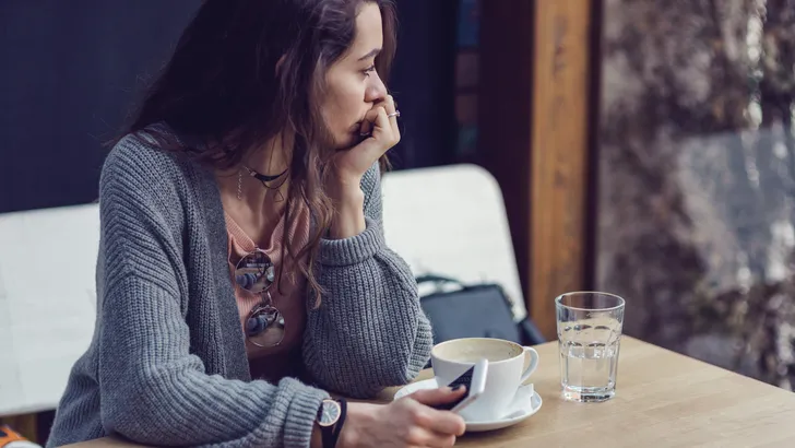 Woman sitting alone, having coffee and texting on her mobile phone