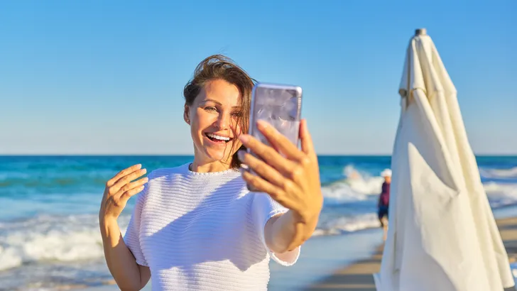 Vrouw houdt telefoon vast op het strand