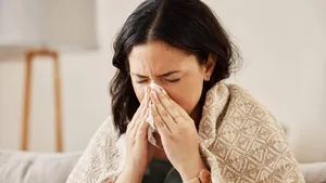 Nose, tissue and sick woman sneezing on a sofa with allergy, cold or flu in her home. Hay fever, allergy and female with viral infection, problem or health crisis in a living room with congestion
