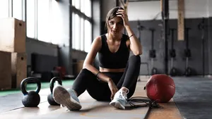 Young woman sitting on floor after her workout and looking down. Female athlete taking rest after fitness training