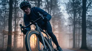 Close-up van een wielrenner die met een racefiets door een scherpe bocht op een natte asfaltweg rijdt, waarbij de band vervormt voor maximale grip op het glanzende wegdek in een winters bos.