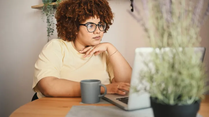 Attractive happy stylish plus size African black woman student afro hair in glasses studying online working on laptop computer at home office workspace. Diversity. Remote work, distance education.