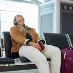 Bored woman, airport and luggage waiting with passport for missed flight, travel or vacation journey in Cape Town. Female traveler sitting in wait for delay departure, boarding plane or immigration