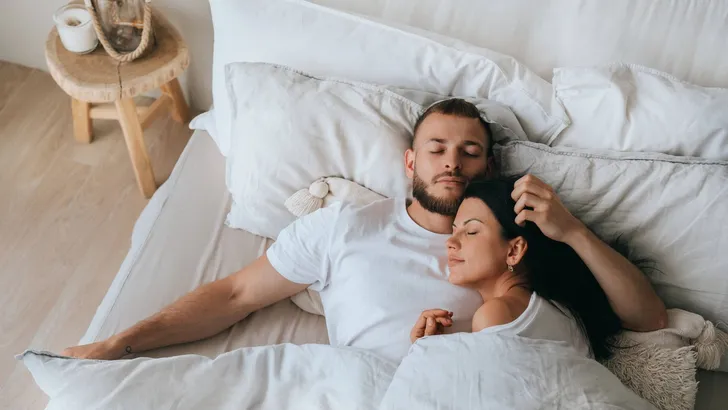 Young caucasian sleeping couple in bed. Handsome beardy European man laying with wife at bedroom enjoying Sunday morning. Calm hispanic young adult woman having nap at hotel with husband.