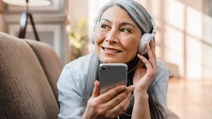 Happy caucasian mature woman listening to the music on the phone on the couch