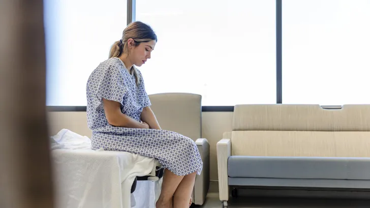 Anxious, sad, young woman wearing hospital gown looks down