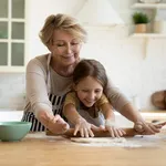 Aged grandma involve small grandkid in rolling dough with pin