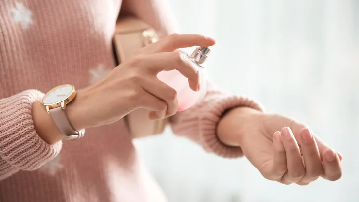 Young woman using perfume indoors, closeup