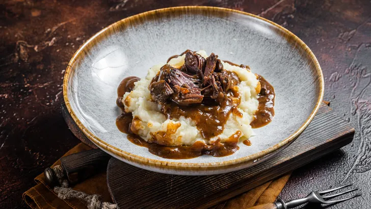 Slow cooked beef cheeks in red wine sauce with mashed potato. Dark background. Top view