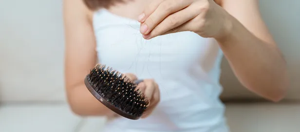 Vrouw haalt losse haren uit een haarborstel. 