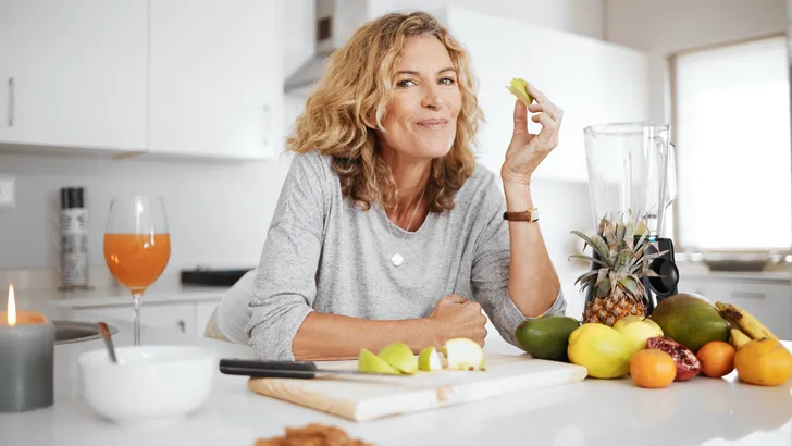 Vrouw staat in keuken en eet gezonde maaltijd die ijzerrijk is.