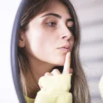 Woman applying cold sore cream on lips in front of mirror