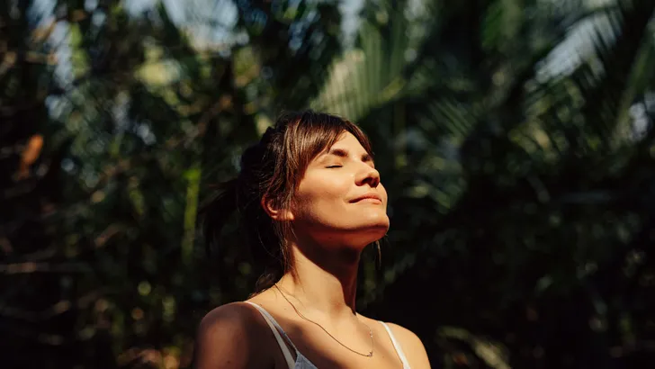 Beautiful Happy Woman Enjoying the Warm Sunlight in a Tropical Public Park