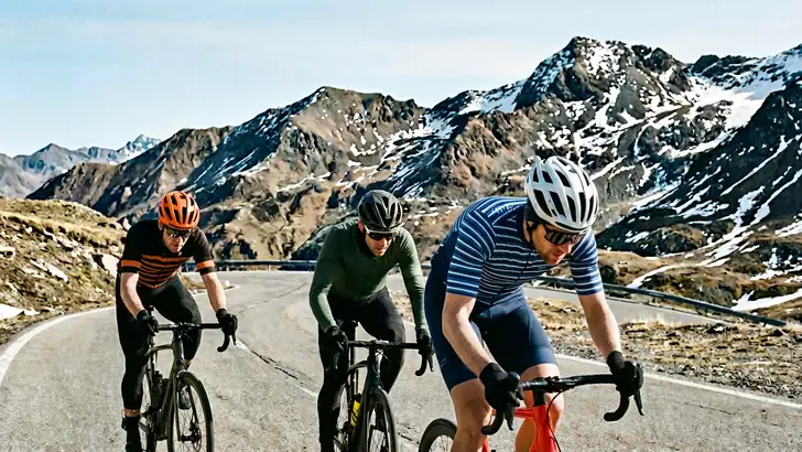Drie amateurfietsers fietsen op een weg hoog in de bergen, ter illustratie van een hoogtestage voor amateurs.