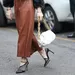 Hoe zwaar mag een handtas zijn? – Streetstyle-foto van vrouw in bruinleren rok met zwarte hakken en witte handtas.