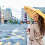 Woman in autumn city. Woman walking on rainy day with yellow umbrella. A portrait of a Long-haired stylish young girl smiling as walking with a umbrella and having fun in the centre of an old city.